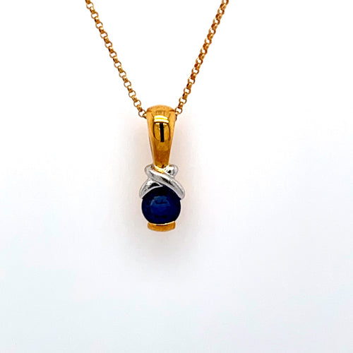 This Beautiful 18 Karat Yellow Gold and White Gold Necklace Features a Beautiful Round Blue Sapphire Gemstone with a White Gold Accent above it, and a High polished Bail. The Chain is an 18 Karat Yellow Gold 16